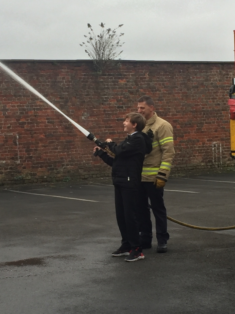 child holding a water hose with a fireman